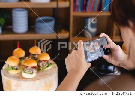A hand taking a photo of a stylish mini burger using a smartphone. A hand taking a photo of a stylish mini burger using a smartphone. 142898751