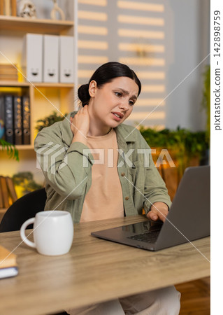 Young woman on home table feeling neck pain and fatigue while working on laptop during study session Young woman on home table feeling neck pain and fatigue while working on laptop during study session 142898759