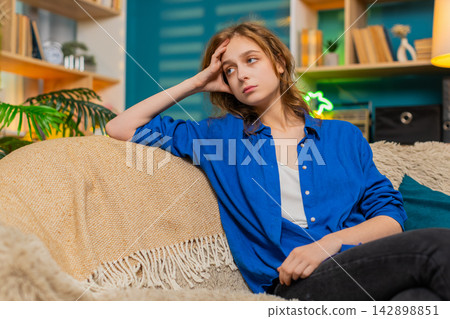 Young woman on home sofa looks tired and emotionally drained with sad stress in cozy home interior Young woman on home sofa looks tired and emotionally drained with sad stress in cozy home interior 142898851