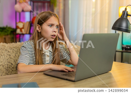 Child girl kid angry at home after losing online quiz game at table with laptop, upset reaction Child girl kid angry at home after losing online quiz game at table with laptop, upset reaction 142899034