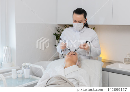 Adult woman receives forehead microcurrent skin therapy in cosmetology clinic rejuvenation session 142899157