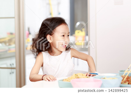 Charming little girl sitting at table during mealtime, looking at camera with a sweet smile, home dining concept. Charming little girl sitting at table during mealtime, looking at camera with a sweet smile, home dining concept. 142899425