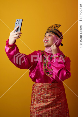 Young Woman In Traditional Southeast Asian Costume And Hijab Taking A Selfie With Smartphone Young Woman In Traditional Southeast Asian Costume And Hijab Taking A Selfie With Smartphone 142899846