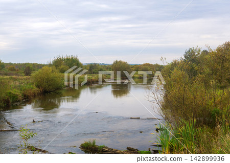 Autumn landscape with the river and trees on a cloudy day. Autumn landscape with the river and trees on a cloudy day. 142899936