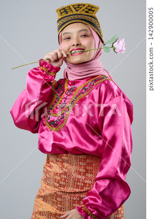 Young Indonesian Asian Woman In Pink Traditional Costume With Hijab And Decorative Headpiece Holding A Rose And Smiling 142900005