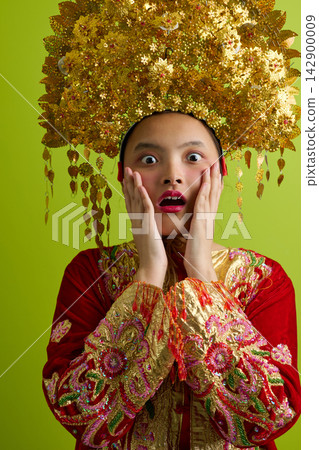 Young Indonesian Asian Woman Wearing Ornate Gold Headdress And Traditional Red Embroidered Costume With Surprised Expression Young Indonesian Asian Woman Wearing Ornate Gold Headdress And Traditional Red Embroidered Costume With Surprised Expression 142900009