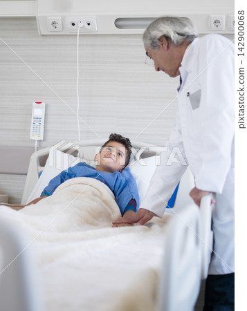 Middle Eastern doctor comforting young boy patient in hospital bed during pediatric checkup and recovery 142900068
