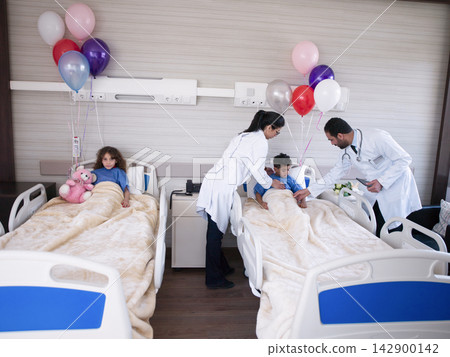 Doctors and nurses caring for young patients in a pediatric hospital room decorated with balloons Doctors and nurses caring for young patients in a pediatric hospital room decorated with balloons 142900142