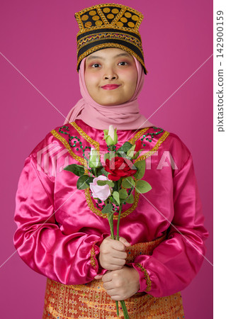 Portrait Of Young Muslim Girl In Pink Traditional Southeast Asian Costume And Hijab Holding Roses 142900159