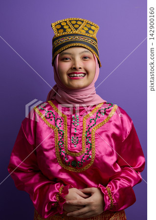 Smiling Young Indonesian Asian Woman in Hijab and Traditional Bright Pink Costume With Decorative Headpiece Portrait 142900160