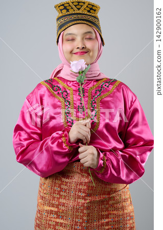 Young Indonesian Asian Woman In Pink Traditional Costume And Hijab Holding A Flower, Smiling With Closed Eyes Young Indonesian Asian Woman In Pink Traditional Costume And Hijab Holding A Flower, Smiling With Closed Eyes 142900162