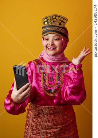 Young Indonesian Asian Woman In Traditional Costume Taking A Smartphone Selfie Wearing Hijab And Smiling 142900174