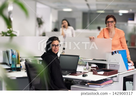 Middle Eastern business women collaborating in a modern open office with friendly colleagues and laptops Middle Eastern business women collaborating in a modern open office with friendly colleagues and laptops 142900317