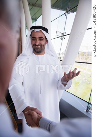 Middle Eastern businessman shaking hands during a friendly business meeting in a modern office space Middle Eastern businessman shaking hands during a friendly business meeting in a modern office space 142900426