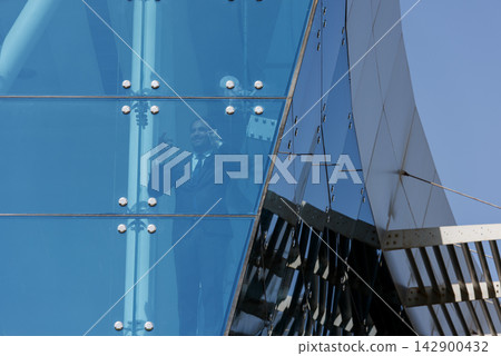 Middle Eastern businessman talking on phone behind glass facade of modern corporate office building Middle Eastern businessman talking on phone behind glass facade of modern corporate office building 142900432