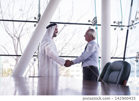Middle Eastern and Western executives shaking hands in a corporate office during business meeting and partnership discussion Middle Eastern and Western executives shaking hands in a corporate office during business meeting and partnership discussion 142900435