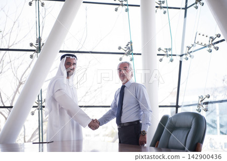 Middle Eastern and Western executives shaking hands in modern corporate office after successful business meeting 142900436