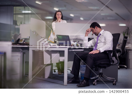 Stressed business professional in modern open-plan office rubbing forehead during a difficult workday Stressed business professional in modern open-plan office rubbing forehead during a difficult workday 142900455