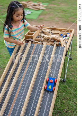 preschool child girl playing with toy car on long wooden track table 142900563
