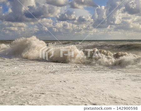Large stormy waves splashing high on a sandy beach covered in thick white foam. Large stormy waves splashing high on a sandy beach covered in thick white foam. 142900598