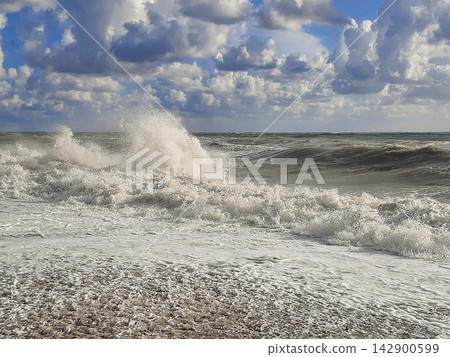 Stormy ocean waves breaking on a pebble beach under a cloudy sky 142900599