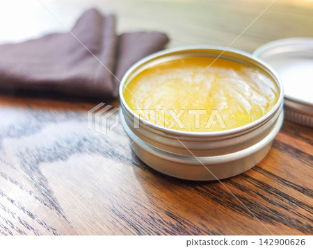 Close-up of yellow natural wood polish paste in an open round metal tin container. Close-up of yellow natural wood polish paste in an open round metal tin container. 142900626
