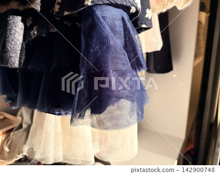 Close-up of children's dresses hanging in a closet in the sunlight. wardrobe for a girl Close-up of children's dresses hanging in a closet in the sunlight. wardrobe for a girl 142900748