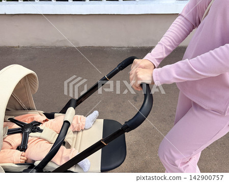 The baby is sleeping in the stroller and is secured with safety straps. The baby is sleeping in the stroller and is secured with safety straps. 142900757