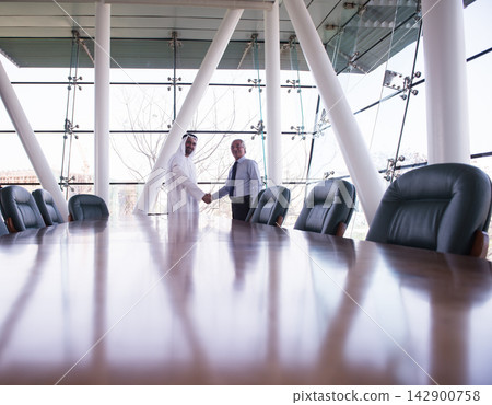 Middle Eastern and Western business partners shaking hands in a modern corporate boardroom during a meeting Middle Eastern and Western business partners shaking hands in a modern corporate boardroom during a meeting 142900758