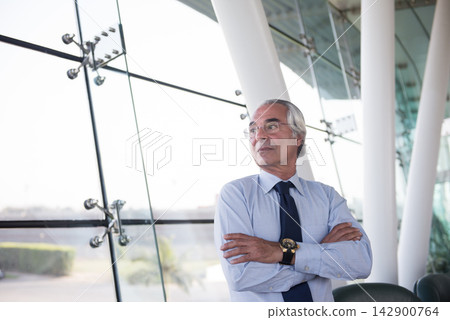 Middle Eastern executive standing confidently in modern corporate office with arms crossed and thoughtful expression Middle Eastern executive standing confidently in modern corporate office with arms crossed and thoughtful expression 142900764