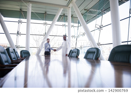 Middle Eastern and Western businessmen shaking hands in modern corporate boardroom during business meeting 142900769