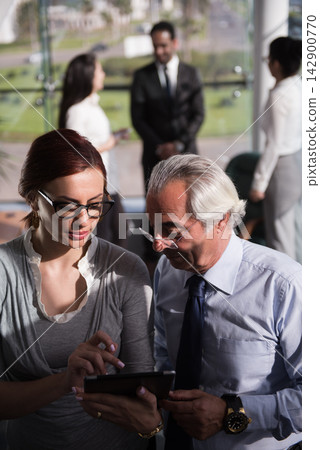 Business colleagues discussing strategy on a tablet during a meeting in a modern open office with mixed generations Business colleagues discussing strategy on a tablet during a meeting in a modern open office with mixed generations 142900770