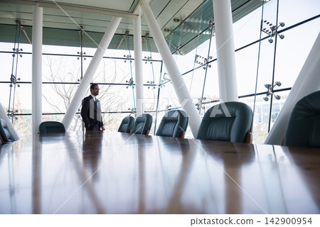 Business executive standing in modern glass boardroom overlooking city during a meeting Business executive standing in modern glass boardroom overlooking city during a meeting 142900954
