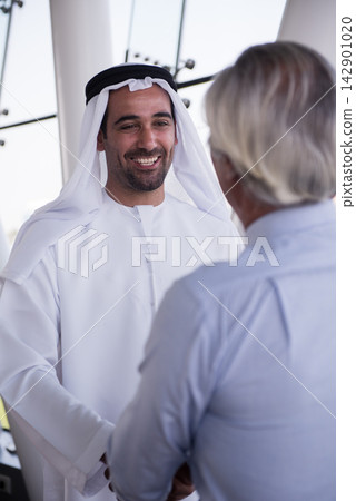 Middle Eastern businessman smiling and shaking hands during a friendly business meeting in modern office Middle Eastern businessman smiling and shaking hands during a friendly business meeting in modern office 142901020