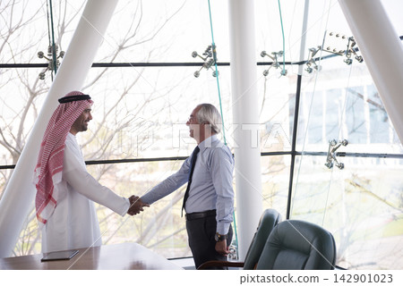 Middle Eastern and Western business partners shaking hands in modern open office during meeting Middle Eastern and Western business partners shaking hands in modern open office during meeting 142901023
