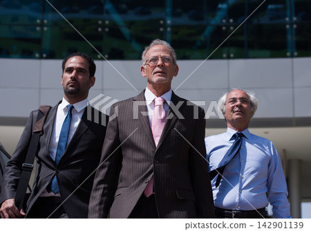 Three confident business executives walking together outside a modern corporate office building Three confident business executives walking together outside a modern corporate office building 142901139