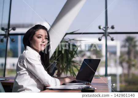 Middle Eastern businesswoman working on laptop in modern open-plan startup office during a thoughtful moment 142901140