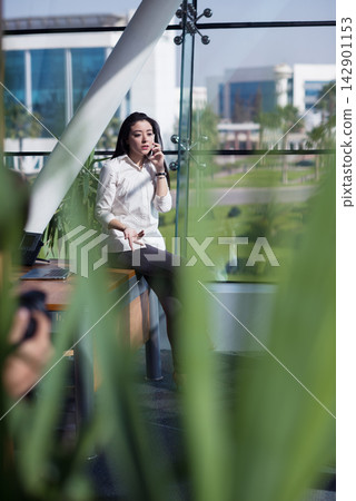Middle Eastern businesswoman on a call in a modern open-plan office with glass and plants 142901153