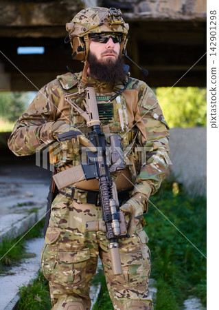 Bearded Soldier In Tactical Camouflage Gear Holding Assault Rifle Near Urban Ruins Bearded Soldier In Tactical Camouflage Gear Holding Assault Rifle Near Urban Ruins 142901298