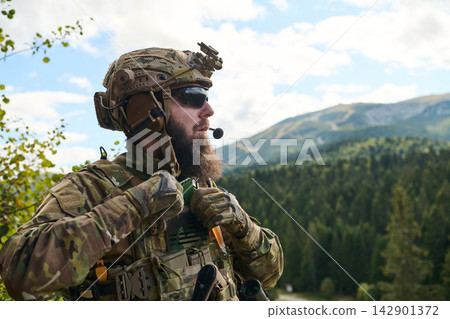 Bearded Soldier in Tactical Gear With Helmet and Radio Overlooking Mountain Forest Landscape Bearded Soldier in Tactical Gear With Helmet and Radio Overlooking Mountain Forest Landscape 142901372
