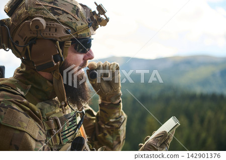 Tactical Soldier Communicating on Radio With Notebook in Mountain Forest During Military Operation Tactical Soldier Communicating on Radio With Notebook in Mountain Forest During Military Operation 142901376