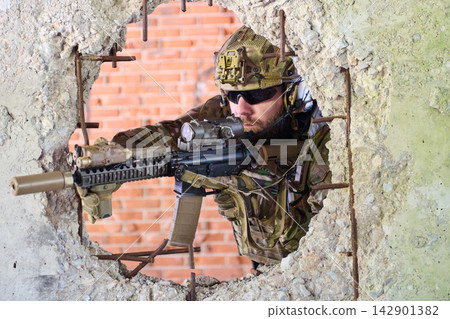 Tactical Soldier Aiming Assault Rifle Through Broken Concrete Wall During Urban Combat Training Mission Tactical Soldier Aiming Assault Rifle Through Broken Concrete Wall During Urban Combat Training Mission 142901382