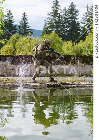 Soldier In Camouflage Tactical Gear Running With Rifle Along Water Edge Splashing Into Pond Soldier In Camouflage Tactical Gear Running With Rifle Along Water Edge Splashing Into Pond 142901404
