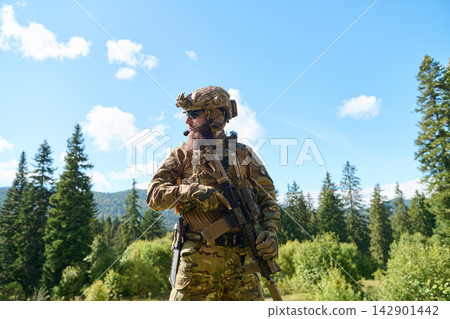 Military Soldier in Camouflage Tactical Gear With Rifle Patrolling a Forested Mountain Landscape Military Soldier in Camouflage Tactical Gear With Rifle Patrolling a Forested Mountain Landscape 142901442