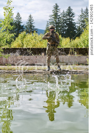 Camouflaged Soldier Standing With Rifle By Pond Reflecting Forest During Outdoor Patrol Exercise Camouflaged Soldier Standing With Rifle By Pond Reflecting Forest During Outdoor Patrol Exercise 142901465
