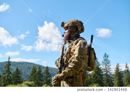 Armed Soldier In Camouflage Tactical Gear Standing Outdoors With Rifle In Mountainous Forest Landscape Armed Soldier In Camouflage Tactical Gear Standing Outdoors With Rifle In Mountainous Forest Landscape 142901498