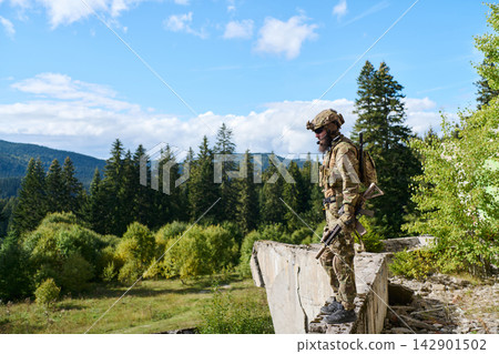 Camouflaged Soldier Standing on Ruined Wall Overlooking Forested Mountain Landscape With Tactical Gear Camouflaged Soldier Standing on Ruined Wall Overlooking Forested Mountain Landscape With Tactical Gear 142901502