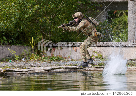 Soldier in Tactical Gear During Military Training Exercise Near Water With Rifle and Splash Soldier in Tactical Gear During Military Training Exercise Near Water With Rifle and Splash 142901565