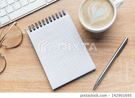 Desk with notepad, keyboard, coffee, pen, and glasses Desk with notepad, keyboard, coffee, pen, and glasses 142901695
