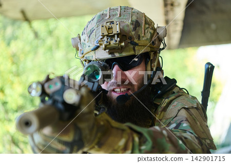 Tactical Soldier in Camouflage Aiming Rifle With Helmet Optics and Comms Gear in Close-Up Tactical Soldier in Camouflage Aiming Rifle With Helmet Optics and Comms Gear in Close-Up 142901715